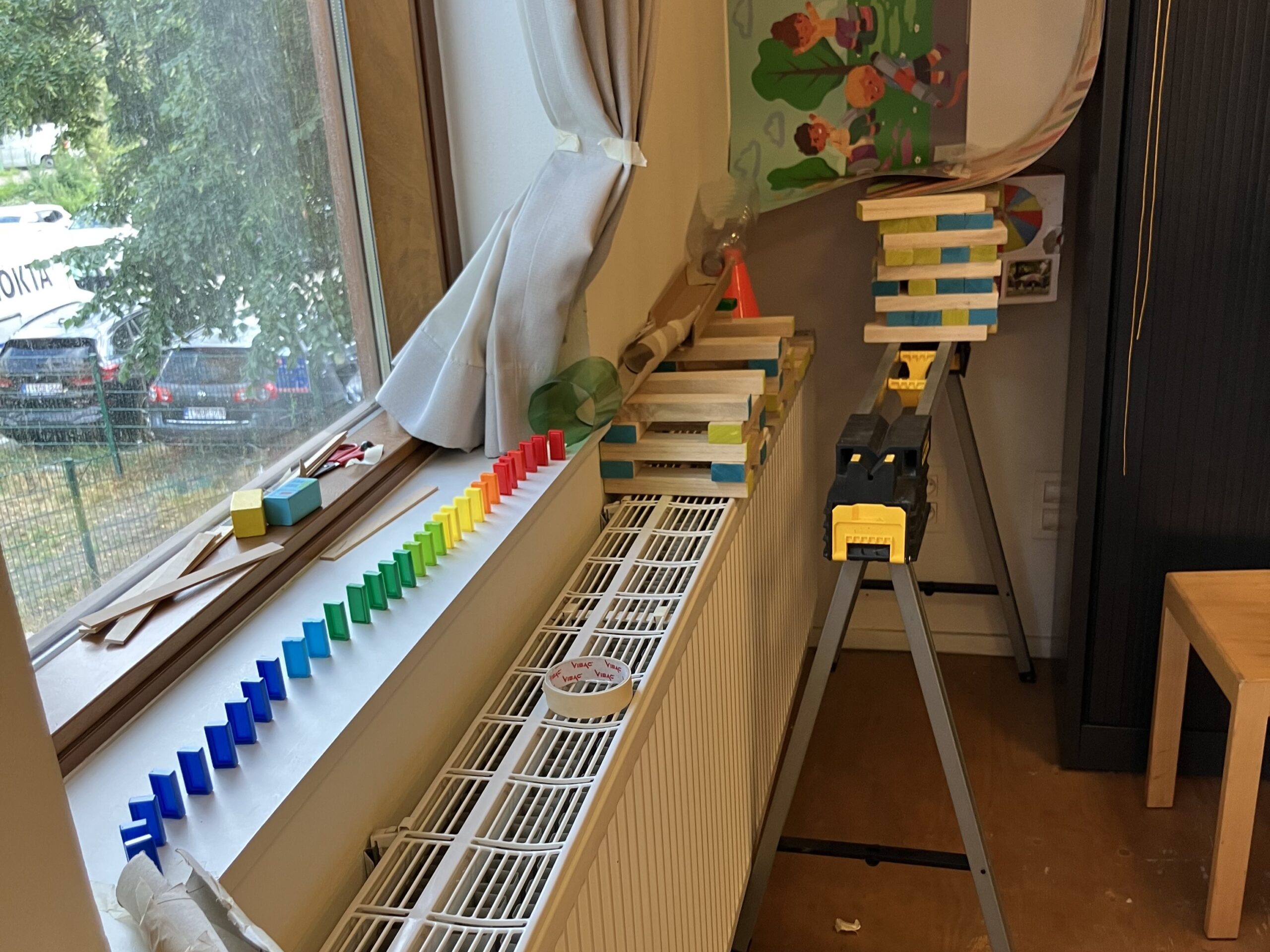 Hoek van een kamer met een diy knikkerbaan vanaf de kast naar de vensterbank, domino's over de vensterbank en de start van een nieuwe knikkerbaan vanaf de vensterbank.