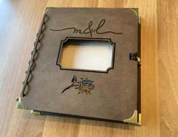 Decoratief boek met houten kaft, initialen in handschrijft, decoratieve roos, doorkijkvenstertje, makrame rug en goudkleurige afwerkingen.