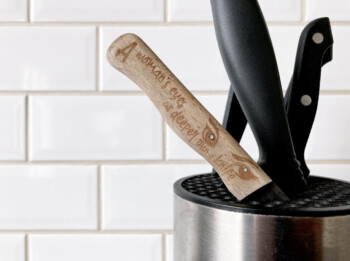 Messenhouder met ondermeer een houten keukenmesje met daarop de quote "A woman's eyes cut deeper than a knife".