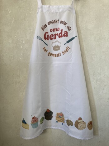 Witte schort met verschillende gebakjes en opschrift "alles smaakt beter als oma Gerde het gemaakt heeft".