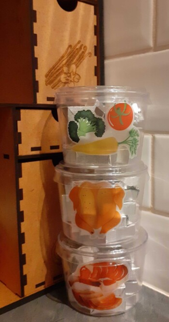 Doorzichtige potjes gevuld met bouillionblokjes en bestickerd met illustraties van groenten, kip en vlees.
