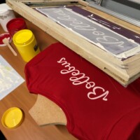 Pas gedrukt rood T-shirt in een zeefdruk set-up, omgeven door zeefdrukinkten.